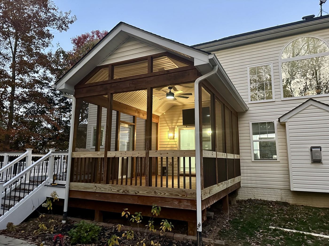 A finished screened porch and stained deck lit up at dusk