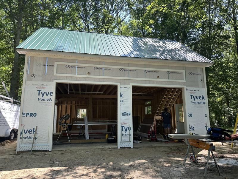 A detached outbuilding under construction with a green metal roof